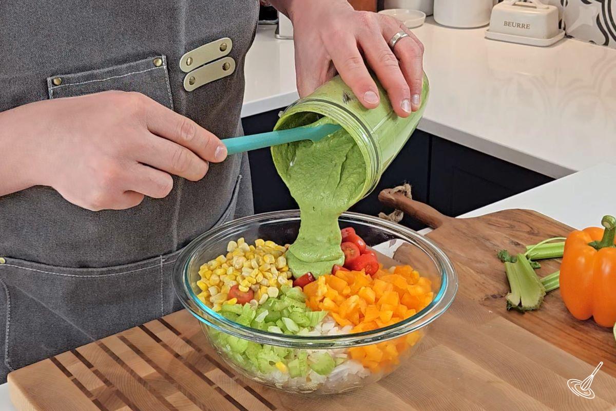 Someone pouring Cilantro Lime dressing over a bowl of pasta salad.