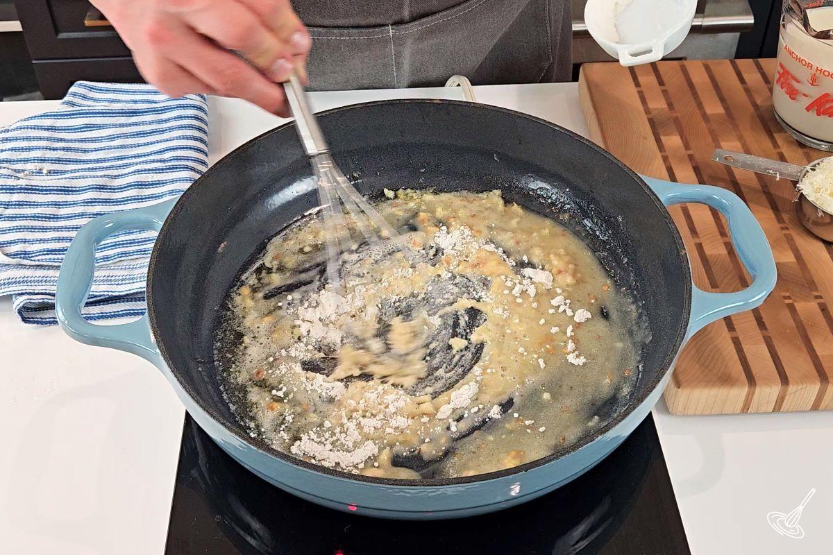 Someone whisking flour into melted butter inside of a skillet.