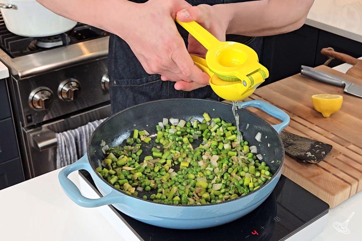 Someone adding lemon juice to a large pan with fried vegetables.