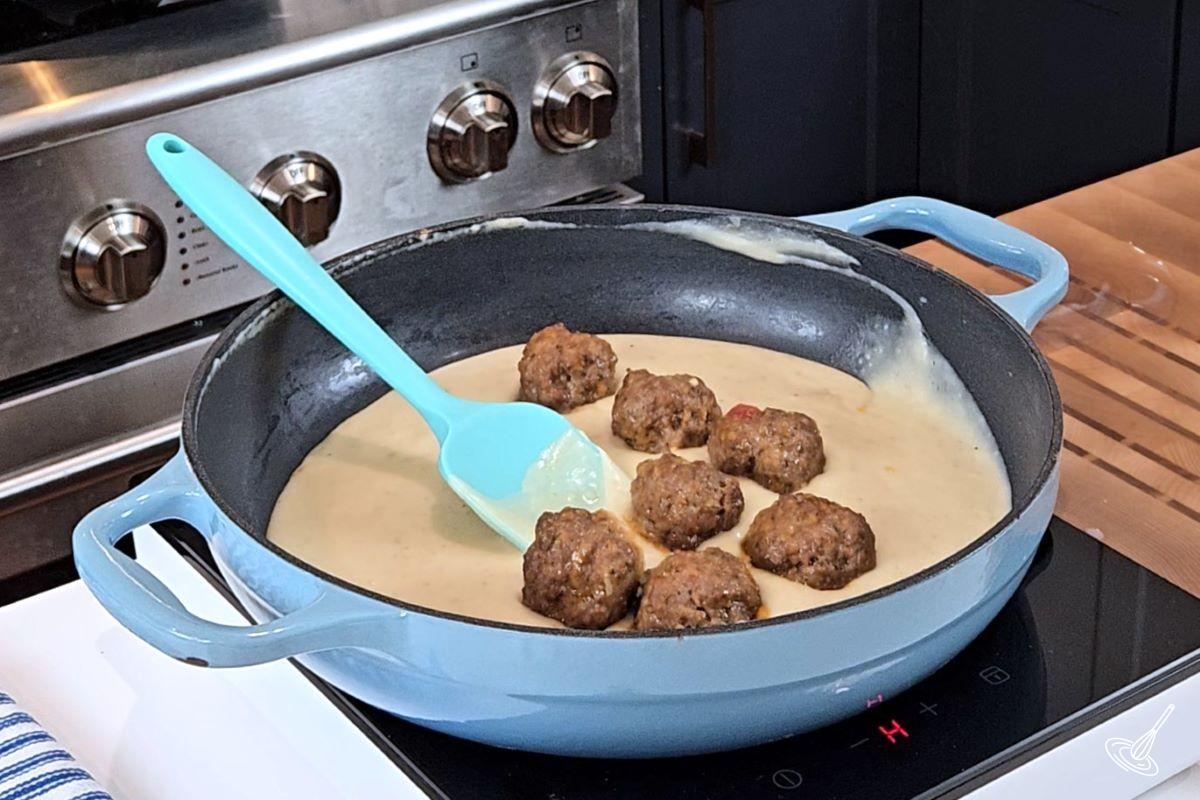 Cooked meatballs in a large skillet with alfredo sauce. 