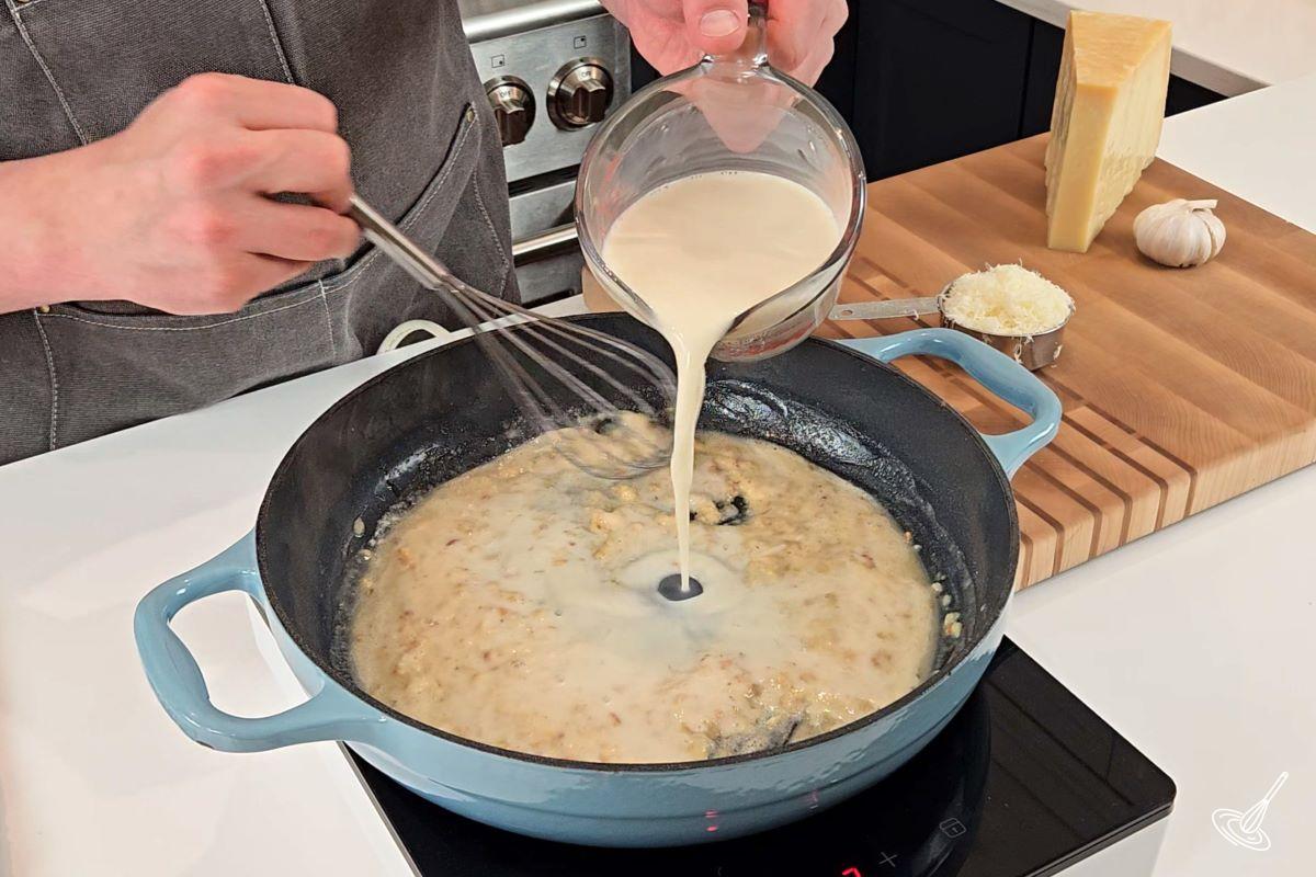 Someone pouring milk into a skillet with melted butter. 