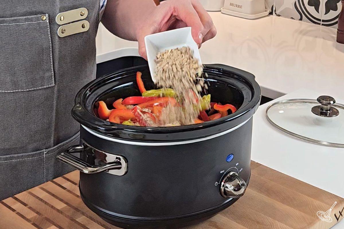 Someone sprinkling onion soup mix in a slow cooker containing meatballs.