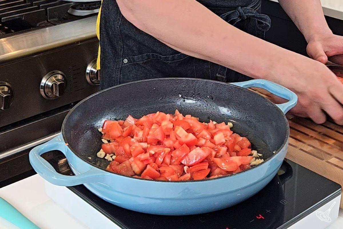 Cubed tomatoes and garlic cooking in a skillet.