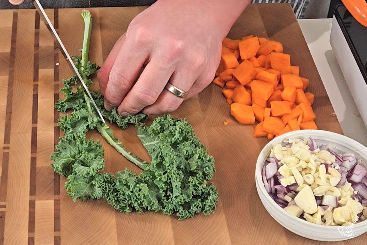 Someone cutting the stem out of a leaf of kale.