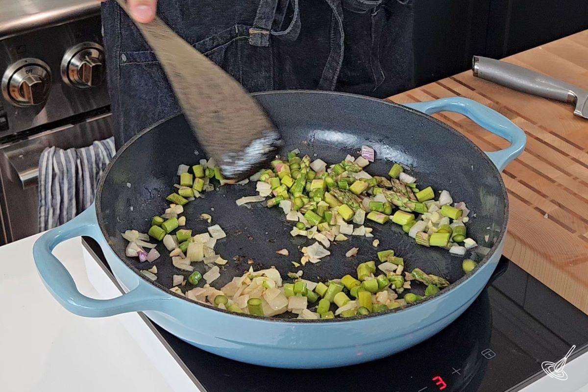 Asparagus, onion, and garlic cooking in a large pan.
