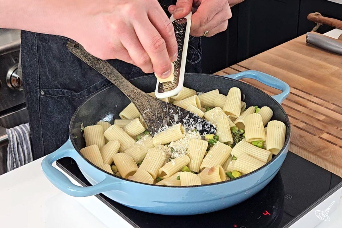 Someone grating parmesan cheese over pasta primavera.