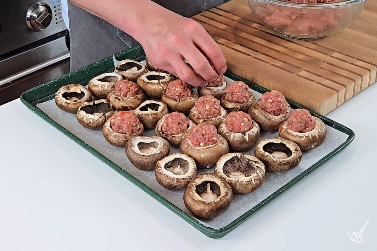 Someone placing shaped meatballs inside cremini mushrooms. 