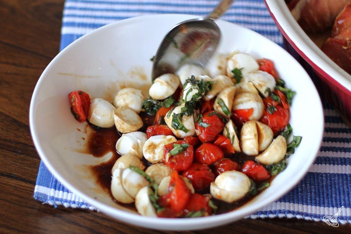 Someone stirring a caprese salad in a bowl.
