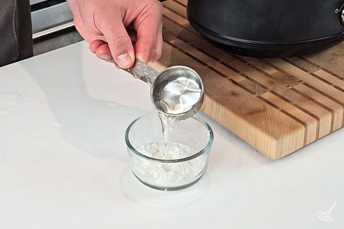 Someone adding water to cornstarch in a small container.