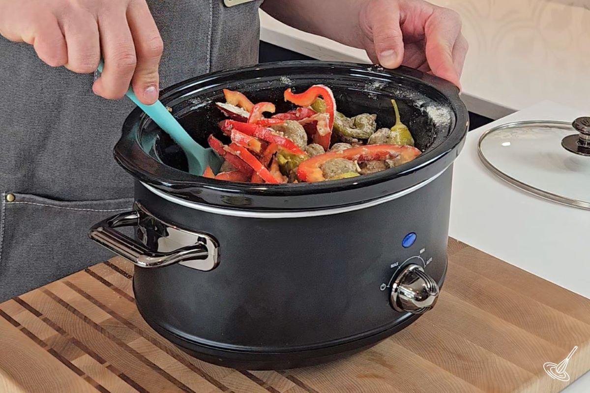 Someone stirring ingredients in a slow cooker with a spatula.
