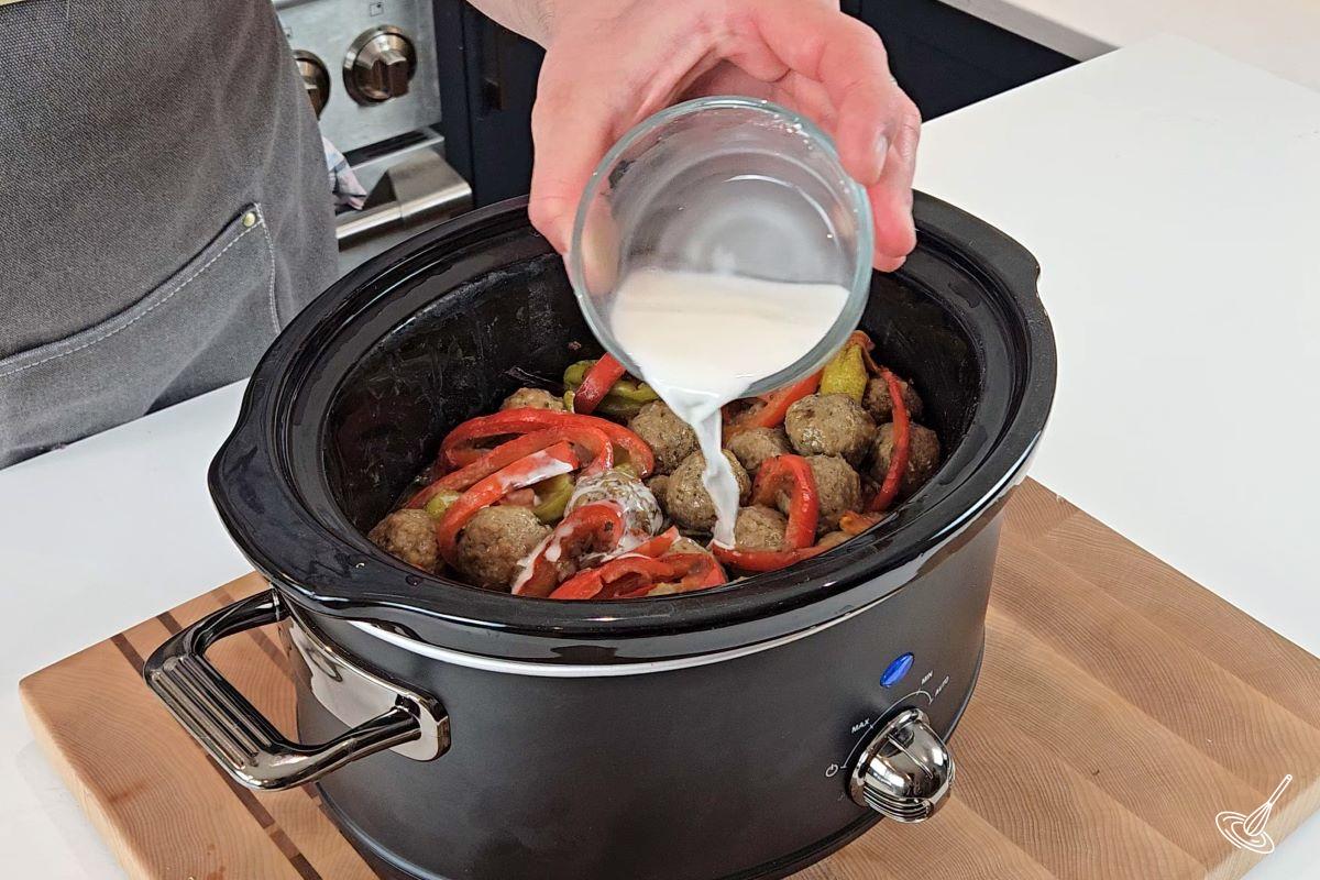 Someone pouring a cornstarch slurry over cooked Mississippi Meatballs in a slow cooker.