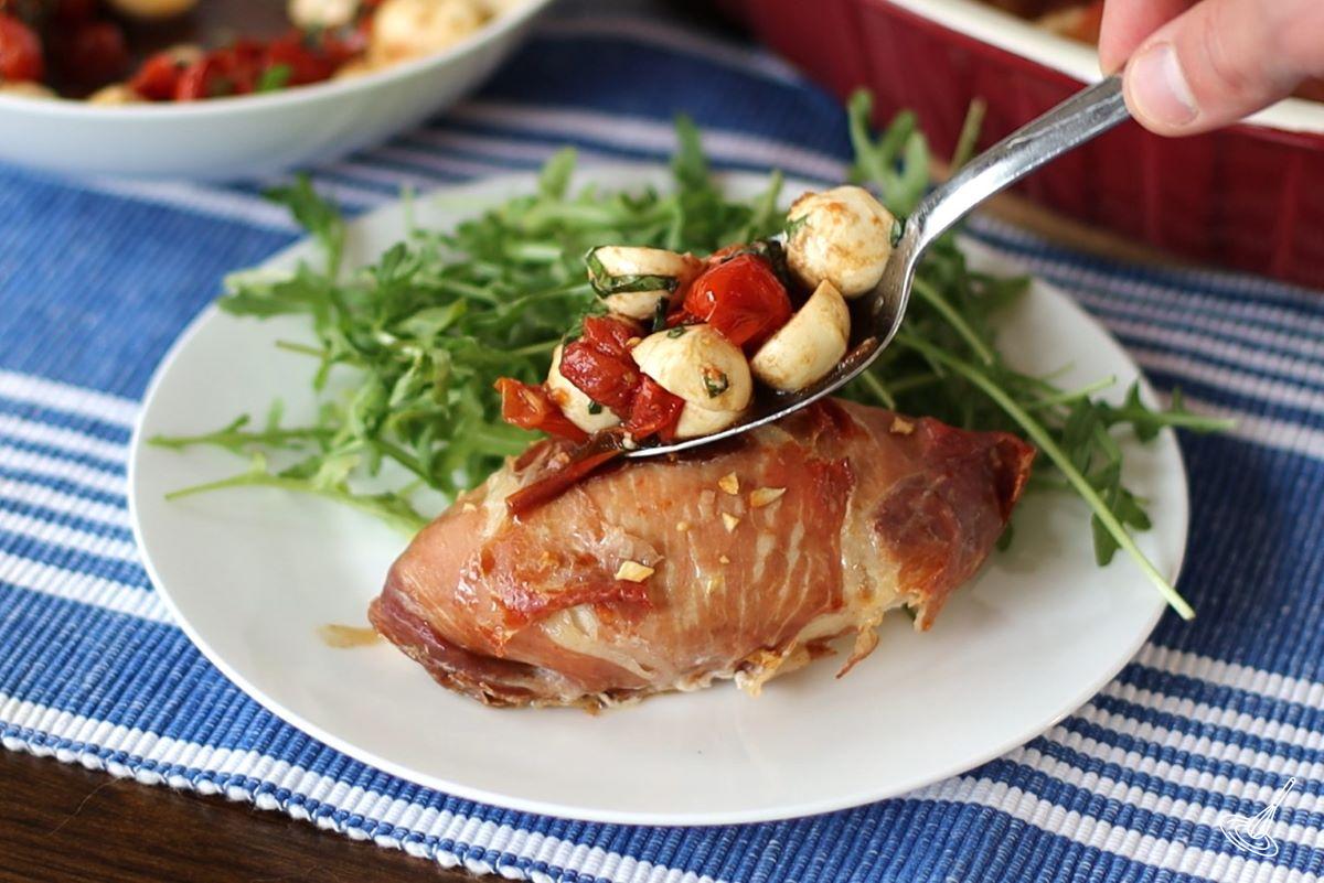 Someone spooning caprese salad over saltimbocca chicken. 