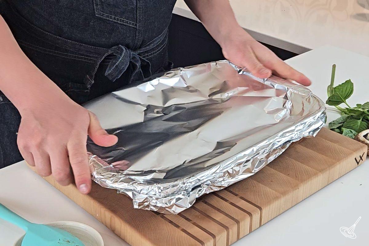 Someone placing aluminum foil over a baking dish. 