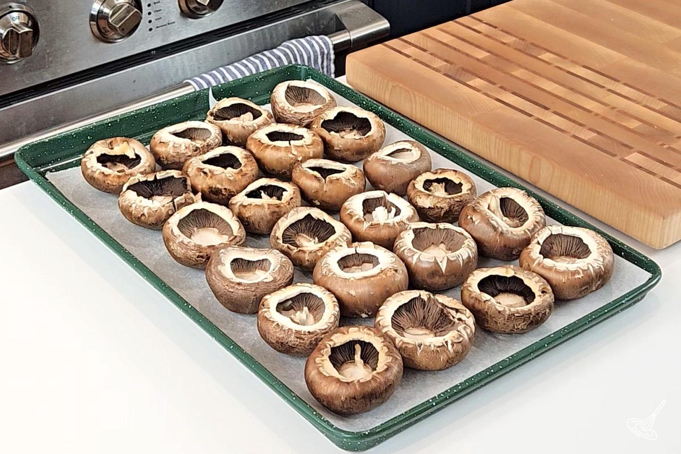A baking tray of cremini mushrooms without stems. 