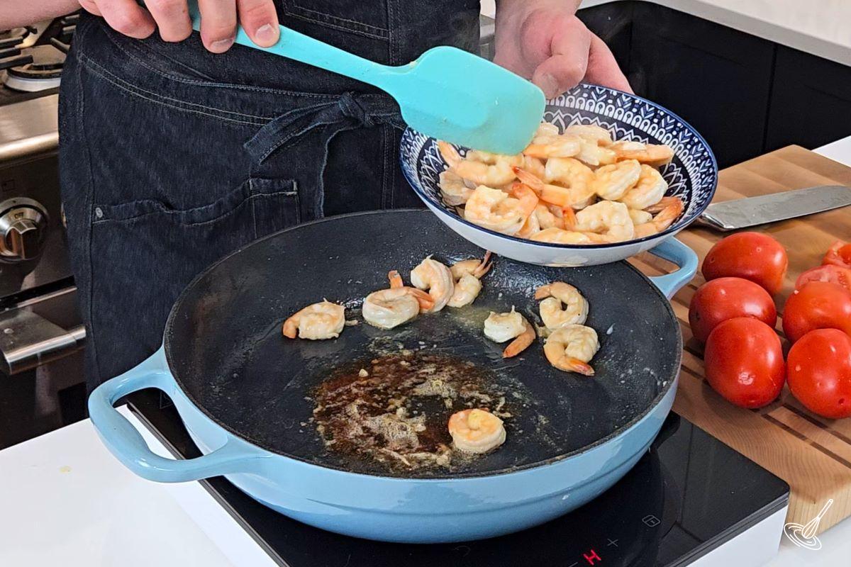 Someone taking cooked shrimp out of a skillet.