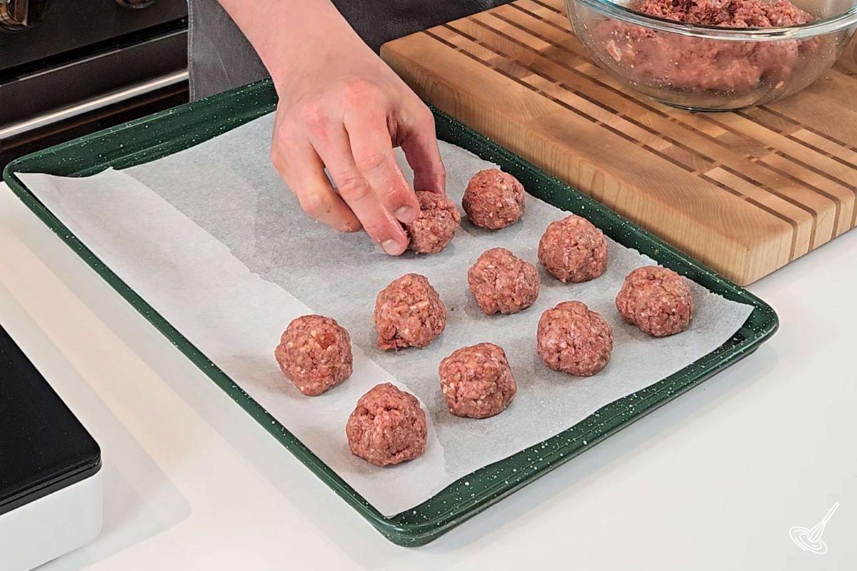 Someone shaping meatballs and placing them on a baking tray.