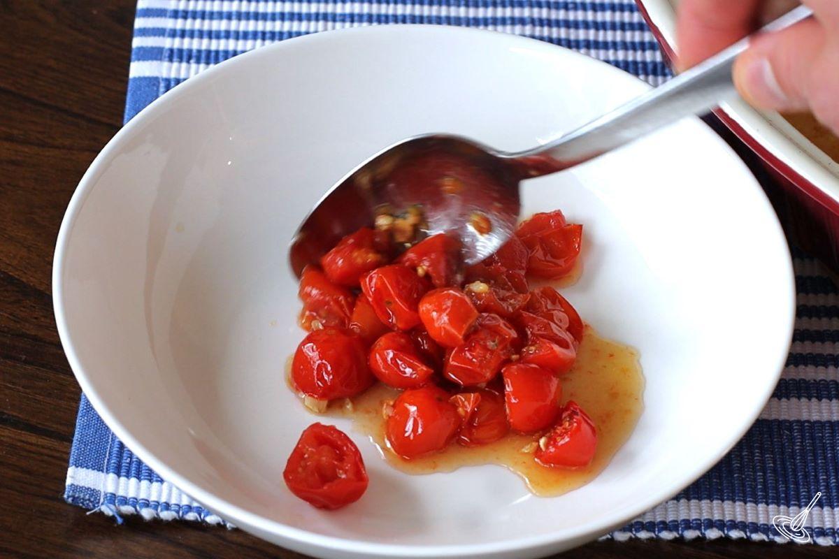 Someone placing roasted tomatoes in a white bowl with a spoon. 