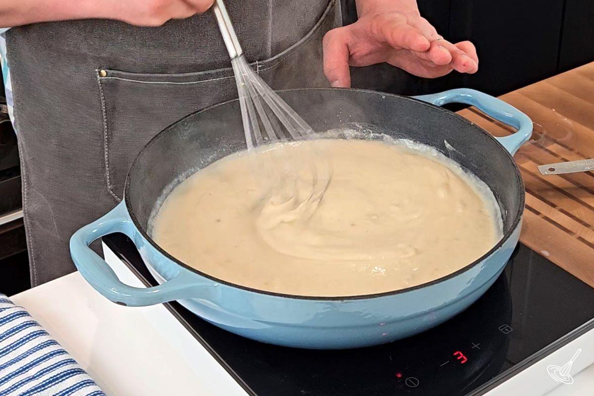 Someone whisking alfredo sauce in a large skillet.