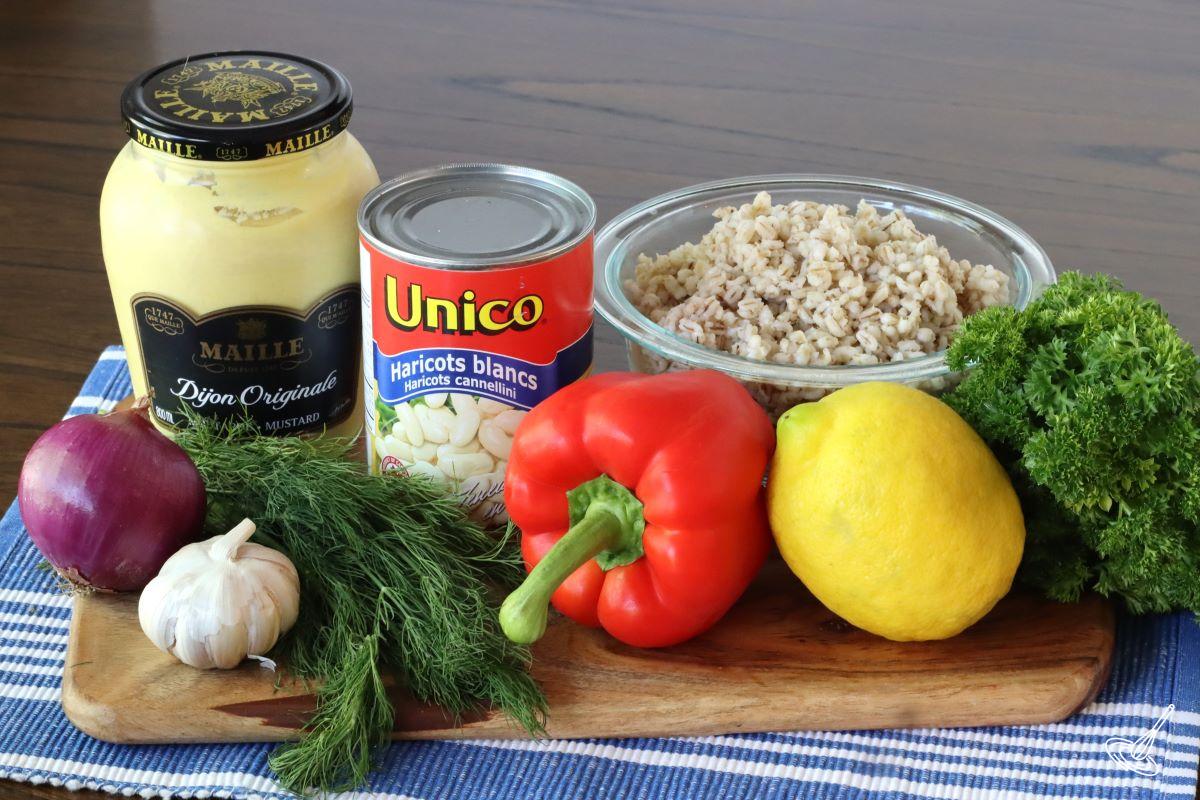 Ingredients to make a salad, including cooked barley, a can of cannellini beans, Dijon, and fresh vegetables. 