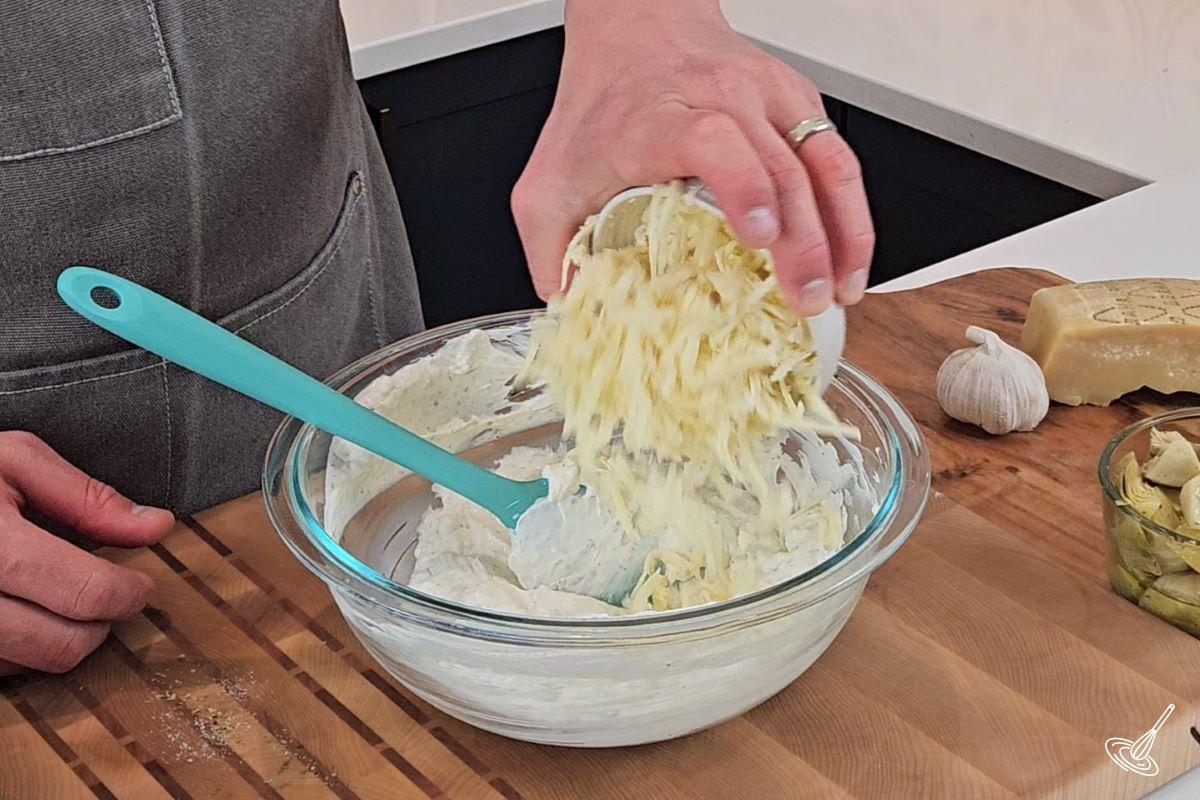 Someone adding grated mozzarella cheese to a large bowl. 