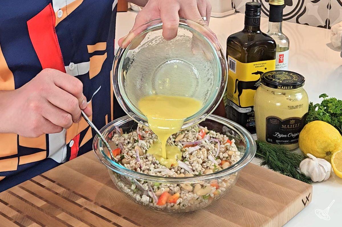 Someone pouring a bowl of dressing into White bean barley salad. 