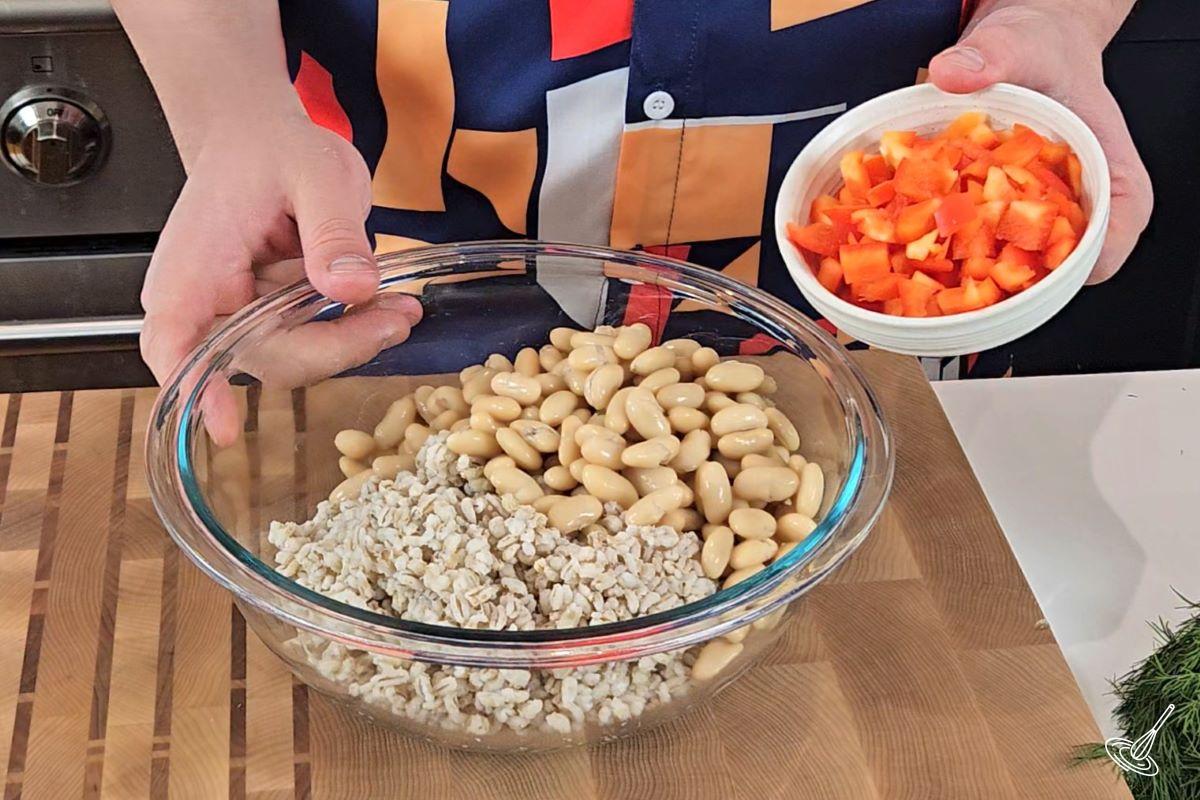 Someone adding diced bell pepper to a bowl of cooked barley and white beans. 