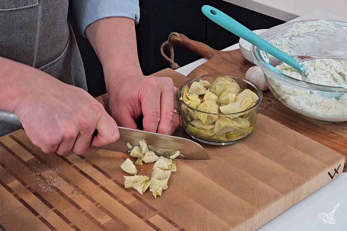 Someone chopping up marinated artichoke hearts into small pieces.