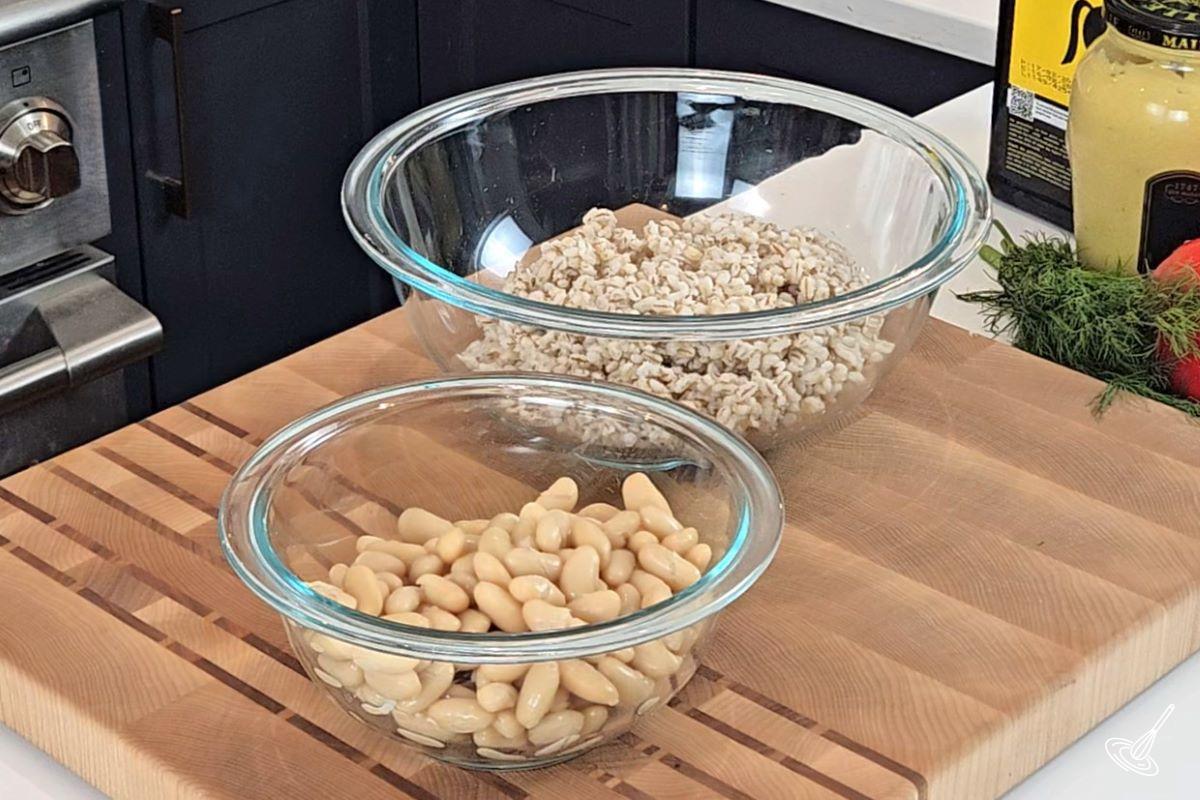 Two bowls on the kitchen counter, one containing cooked barley, and the other drained white beans.