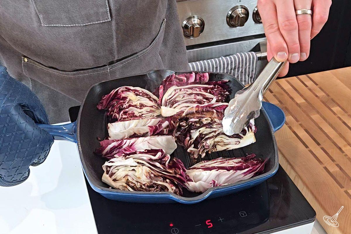 Someone turning over grilled wedges of radicchio in a pan.