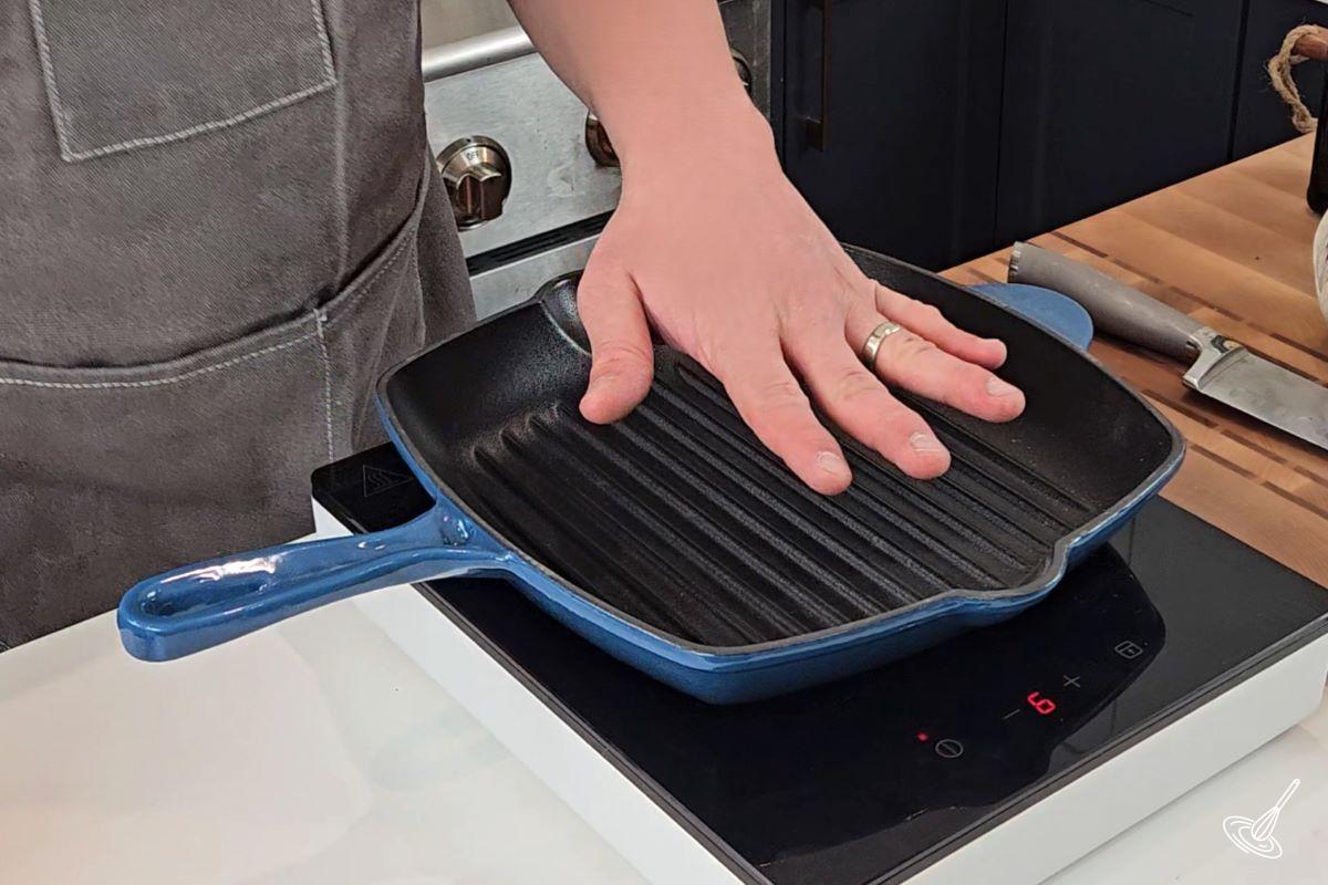 Someone using their hand to feel the temperature of a grill pan. 