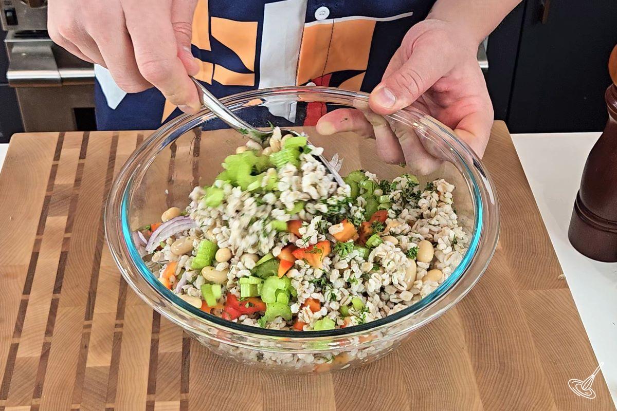 Someone stirring chopped fresh vegetables into a bowl of cooked barley and beans.