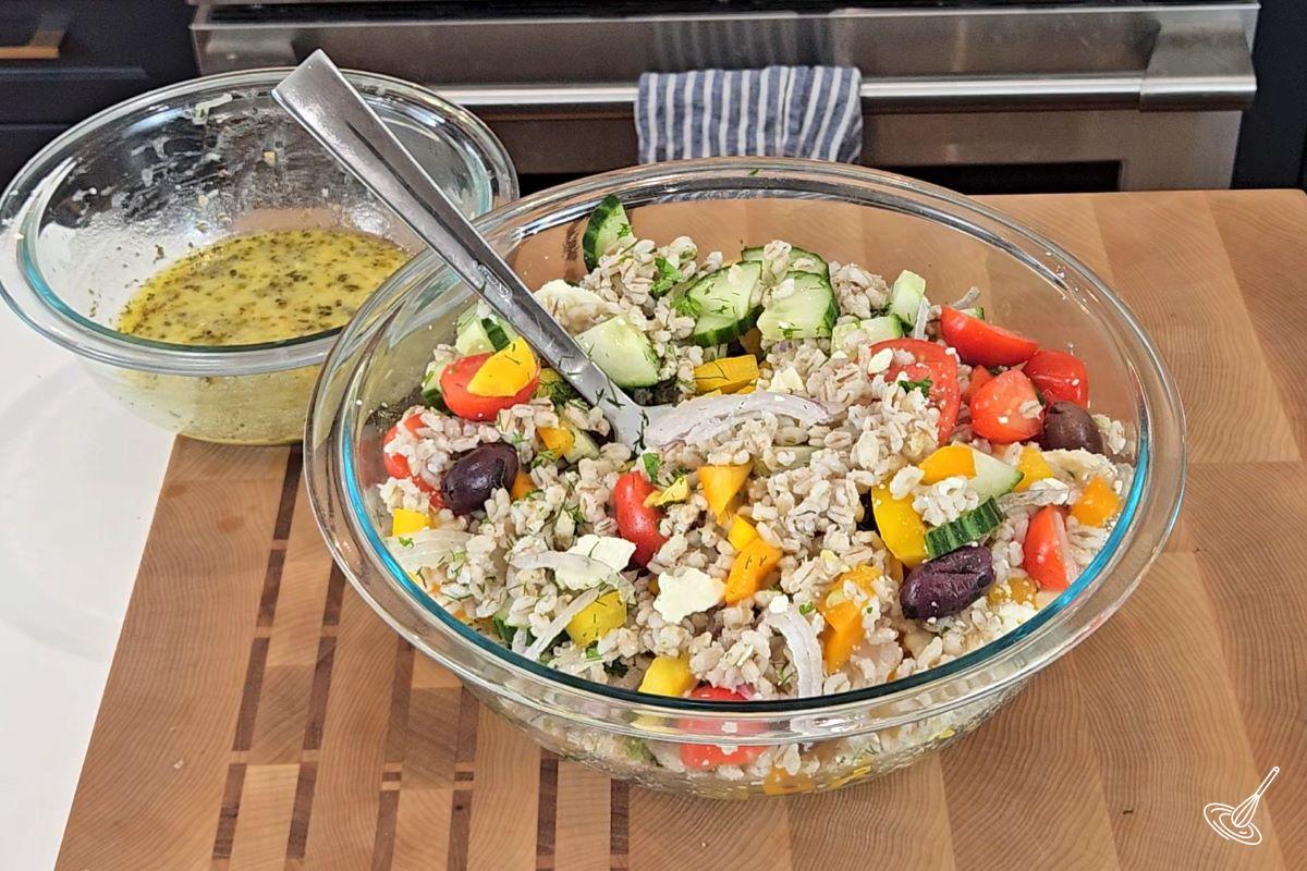 A large bowl of Mediterranean Barley Salad with a smaller bowl of salad dressing on the side. 