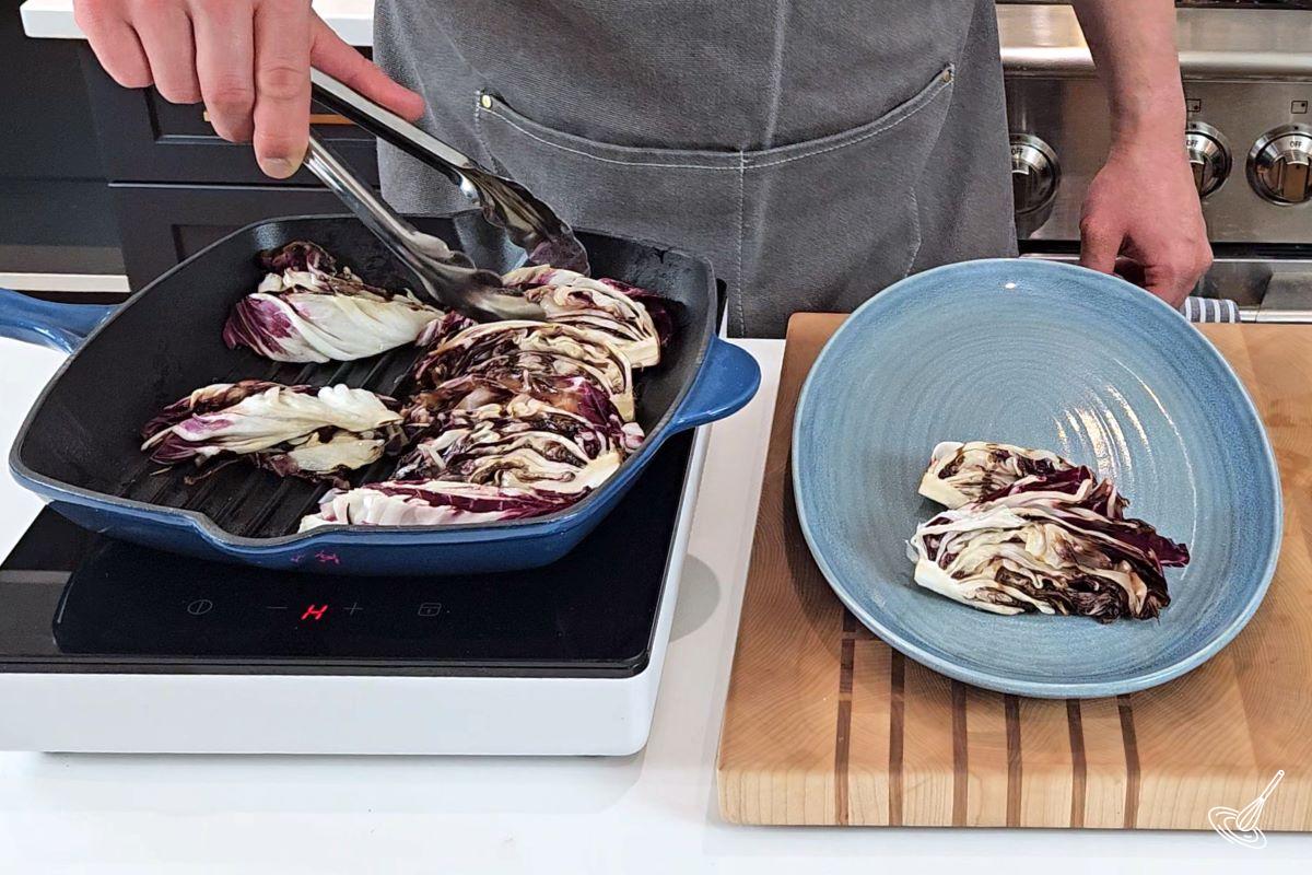 Someone taking grilled wedges of radicchio out of a pan and onto a plate. 