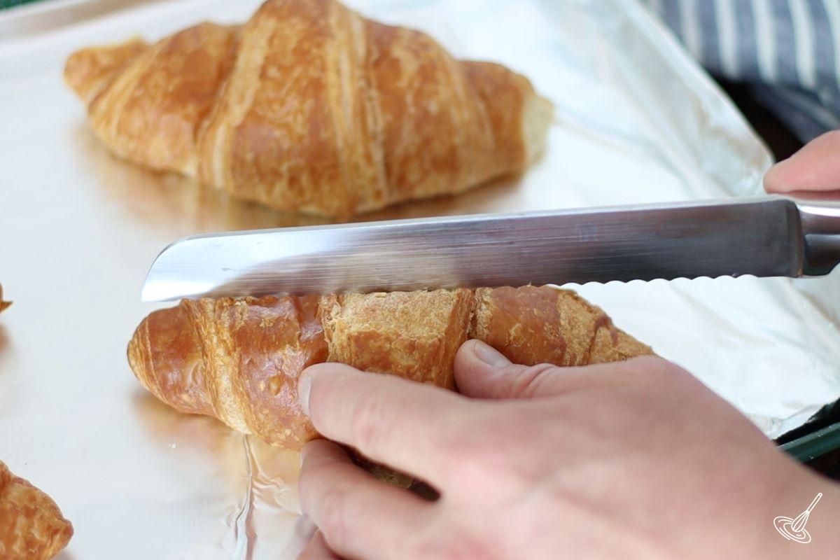 Someone cutting a croissant in half. 