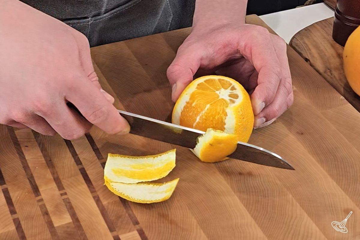 Someone removing the skin from an orange with a knife.