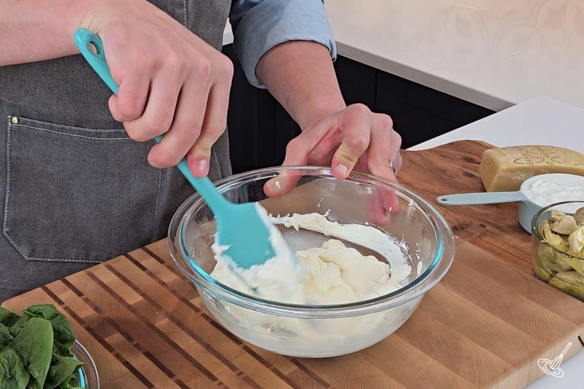 Someone stirring softened cream cheese in a large bowl.