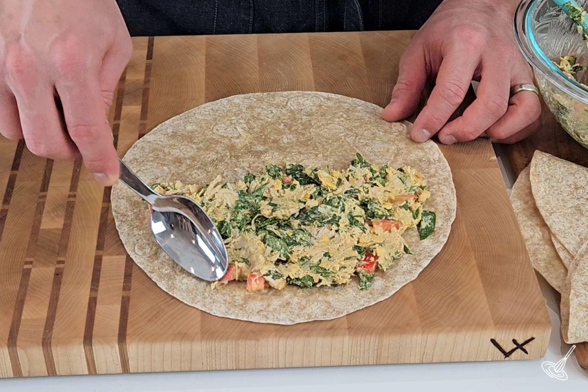 Someone spreading a chicken mixture on a tortilla.