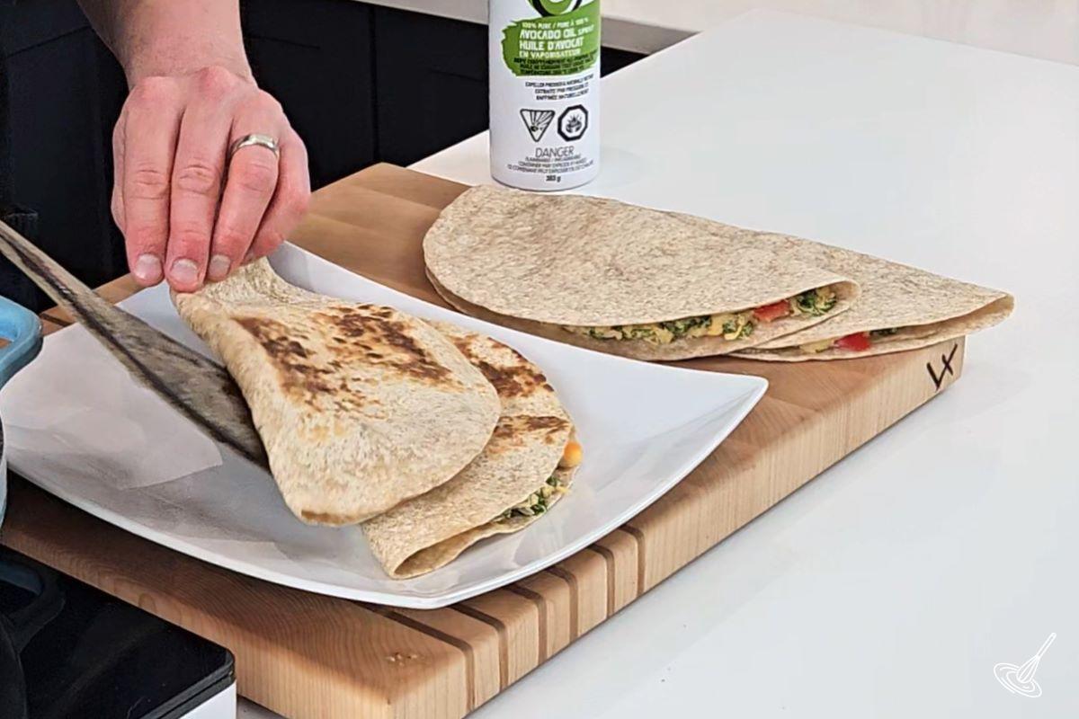 Someone placing a grilled quesadilla on a serving plate.