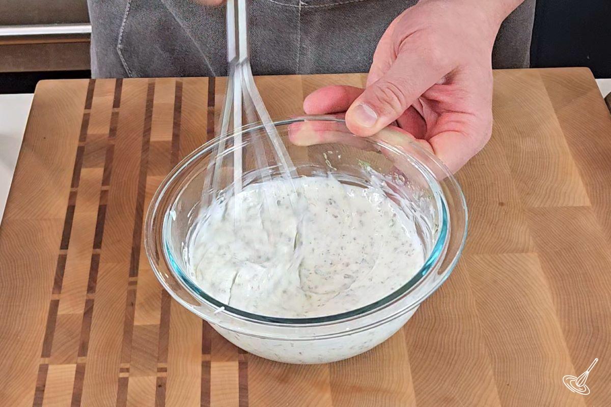 Someone whisking a tarragon salad dressing in a small bowl. 