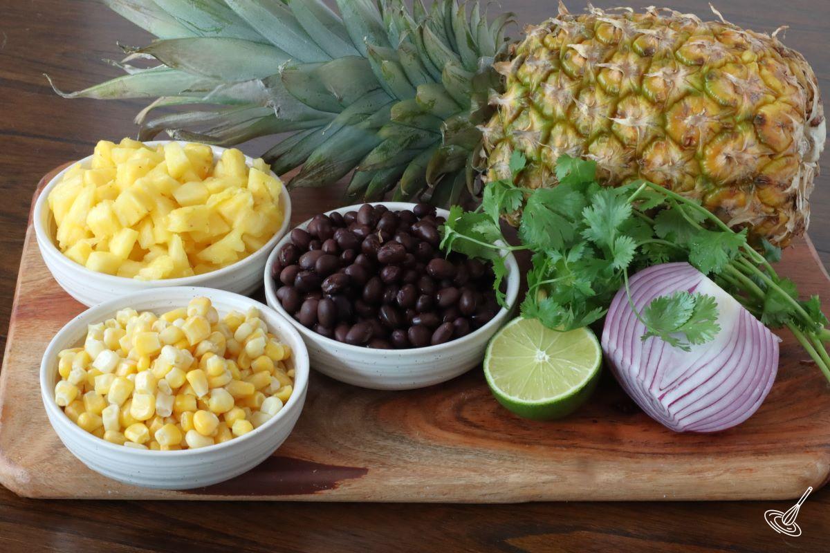 Ingredients on a board including: corn, pineapple, black beans, lime and onion. 