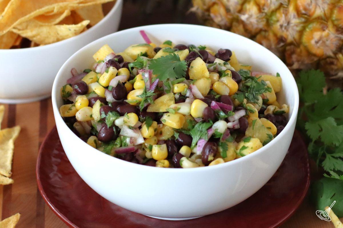 A serving bowl containing Pineapple Corn Salsa, with a side dish of tortilla chips.