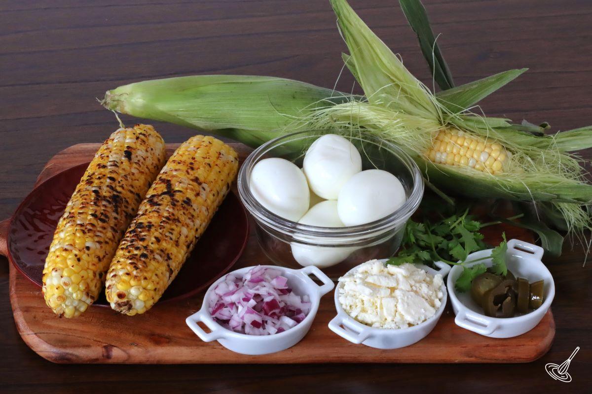 Ingredients on a platter including roasted corn, hard boiled eggs, feta, and red onion.