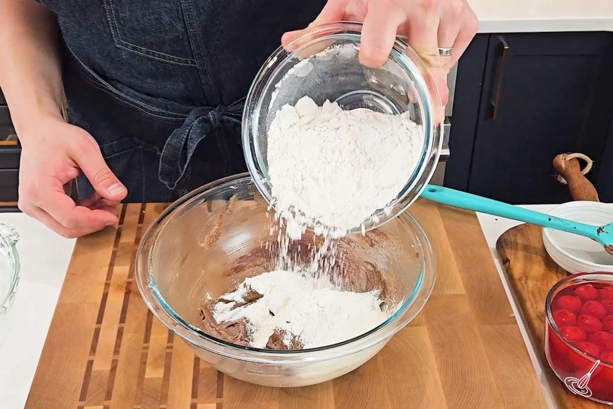Someone adding flour to a bowl of cake batter.