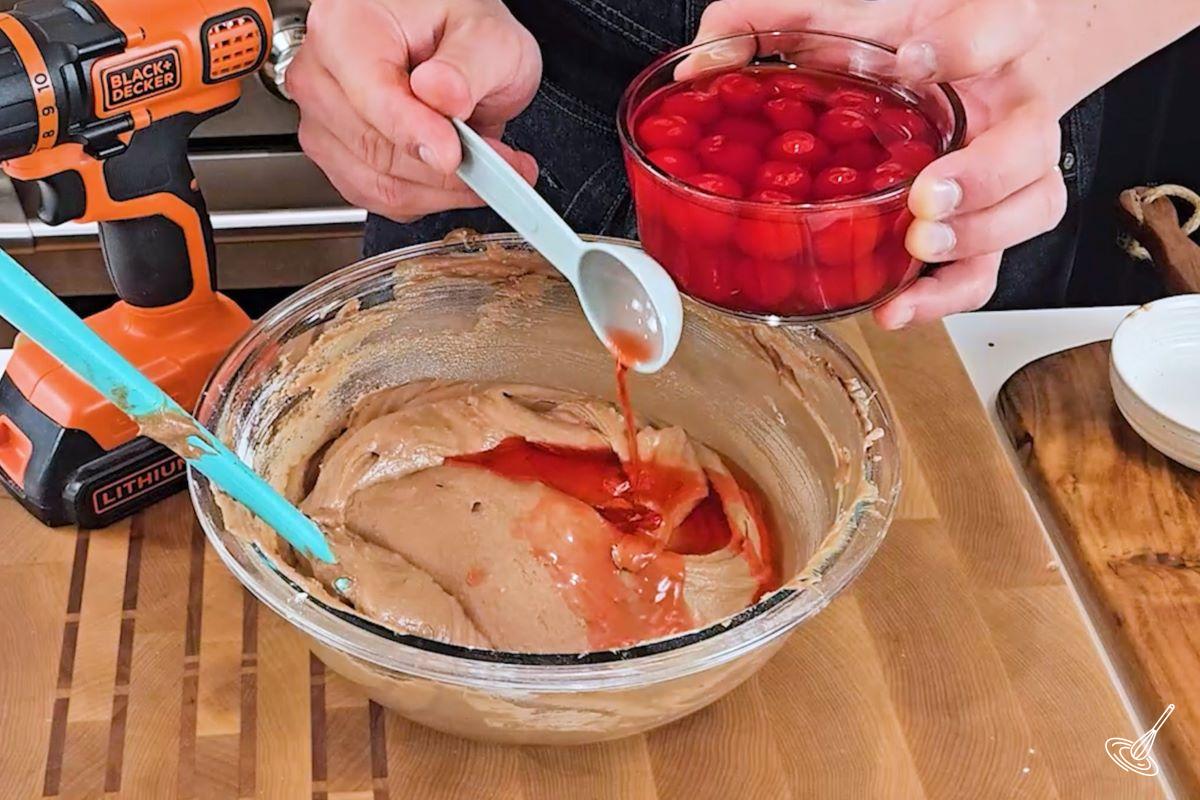 Someone adding cherry syrup to a bowl of cake batter. 