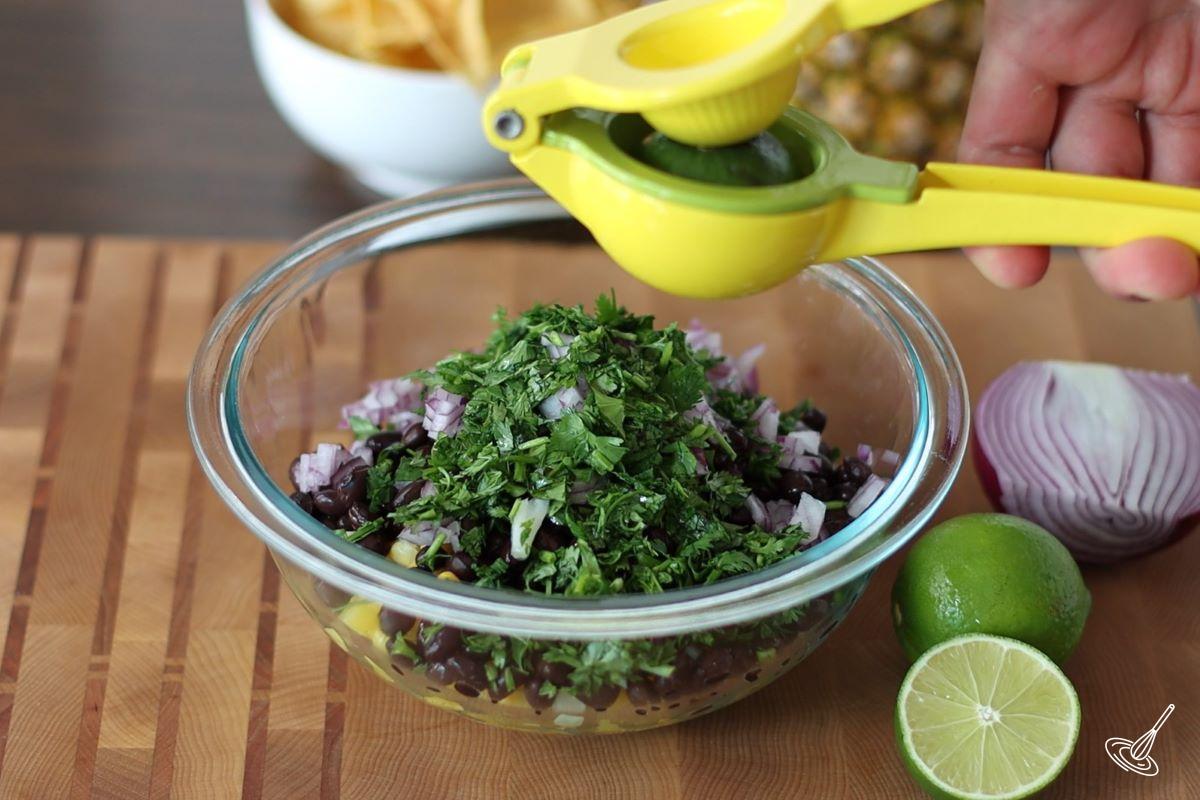 Someone squeezing fresh lime juice in a large bowl of Pineapple Corn Salsa.