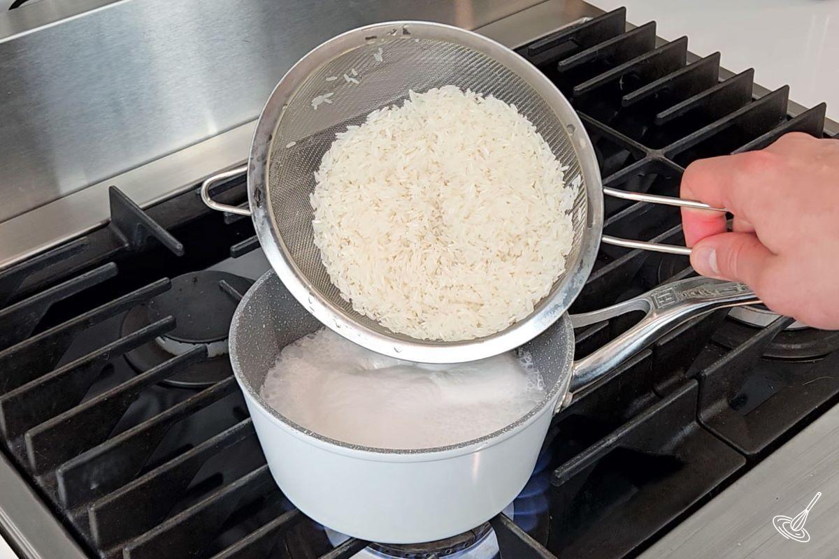 Quelqu'un qui met du riz dans une casserole avec du liquide.