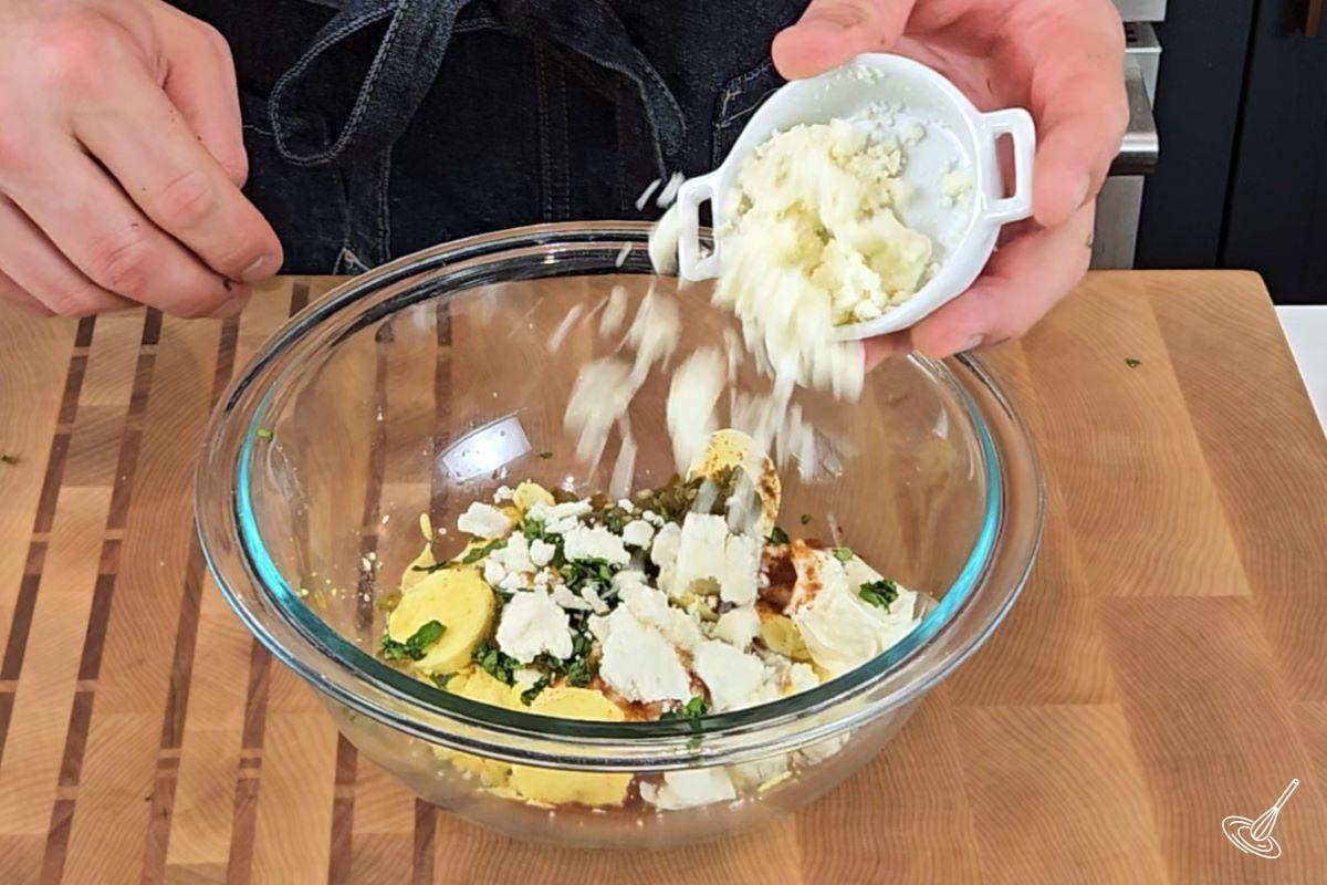 Someone adding feta to a large bowl with egg yolk. 