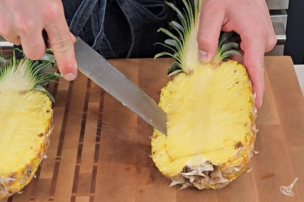 Someone making diagonal cuts in a pineapple half.