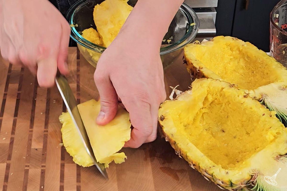 Someone cutting a pineapple into smaller pieces.