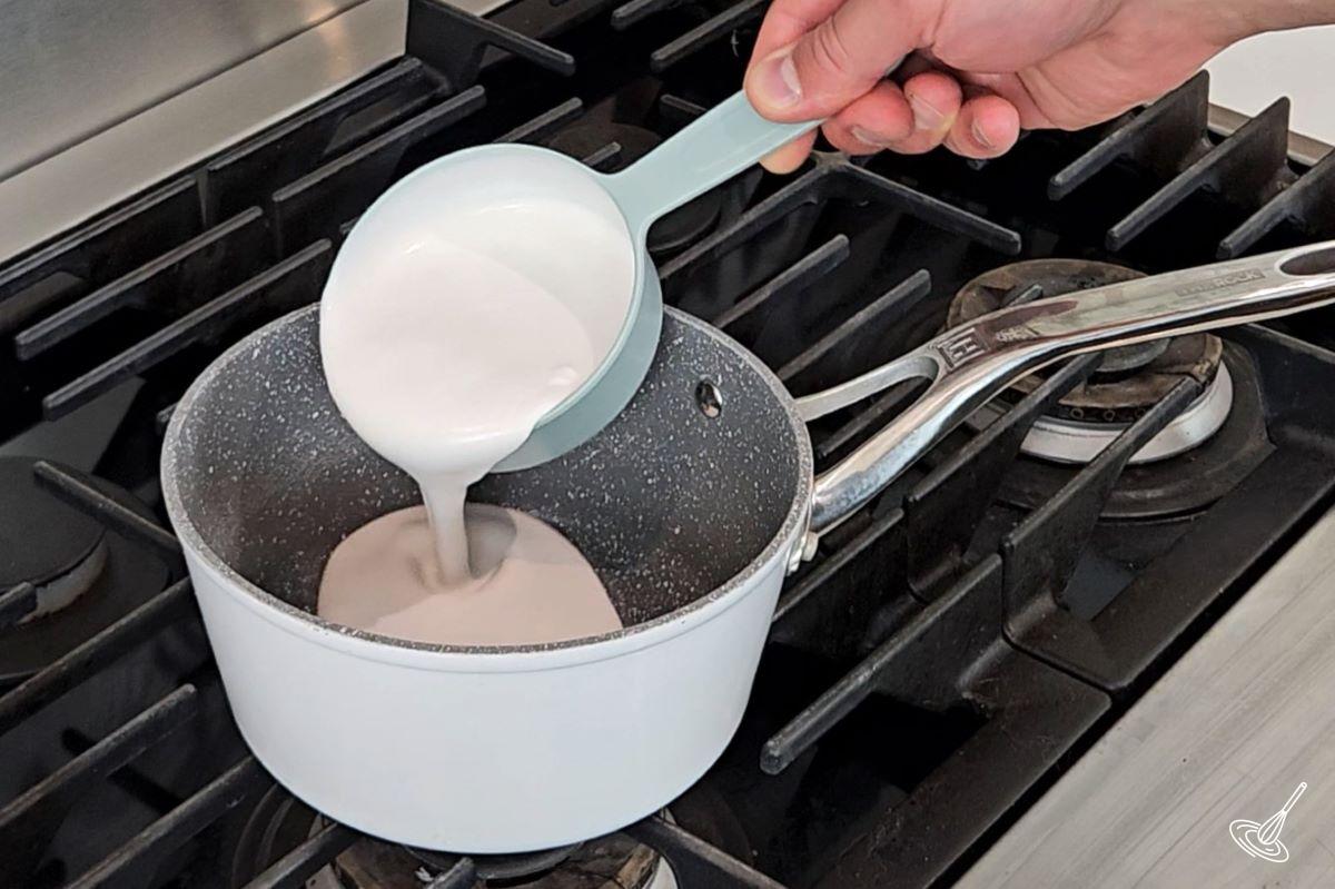 Quelqu'un verse du lait de coco dans une casserole.
